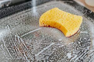 A yellow cleaning sponge wiping soapy foam off a kitchen surface, demonstrating Sola's pro hacks for daily home maintenance.